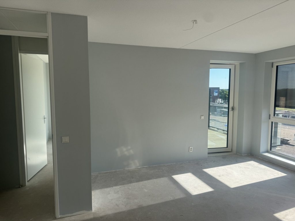 Lichtgrijs afgewerkte woonkamer van een nieuw appartement met een balkondeur en een betonvloer