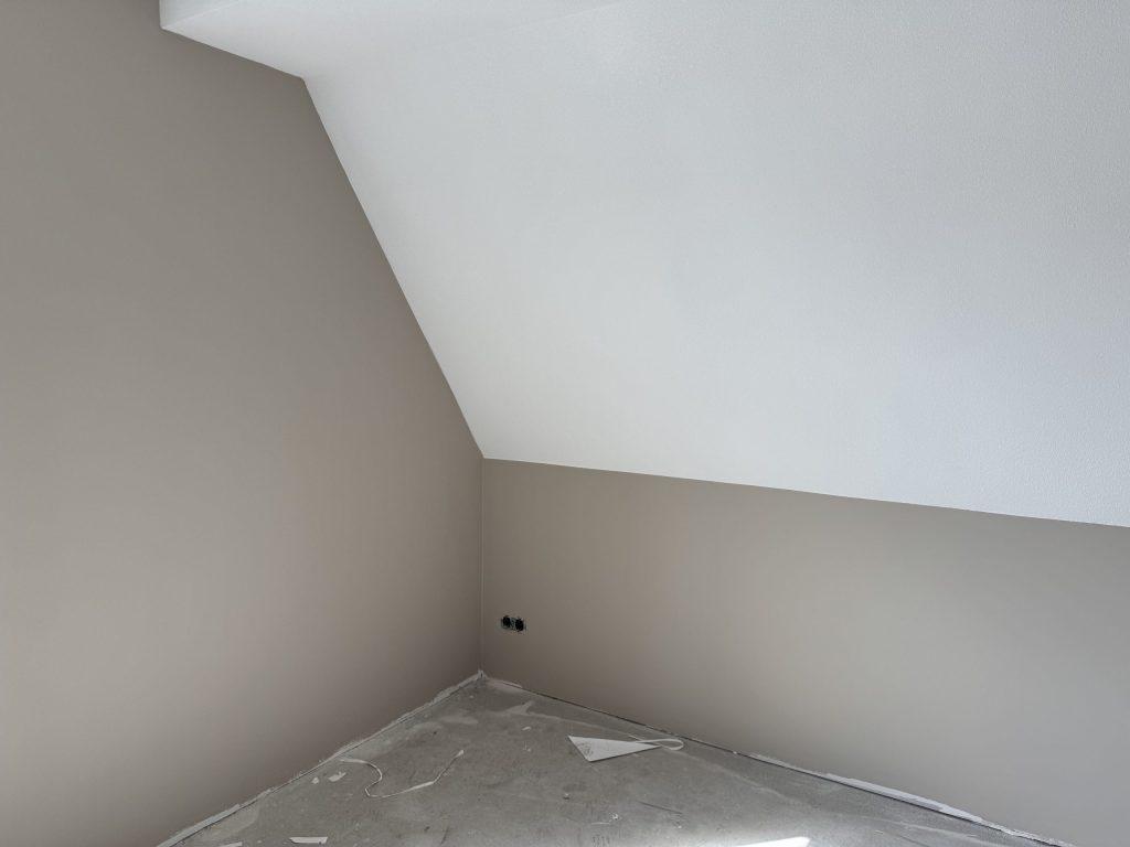 Zolderkamer in een nieuwbouwwoning met een schuine wand, strak afgewerkt in wit en zandkleur